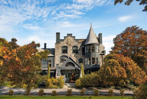 A grand stone mansion with a turret, surrounded by colorful autumn trees and a clear blue sky.