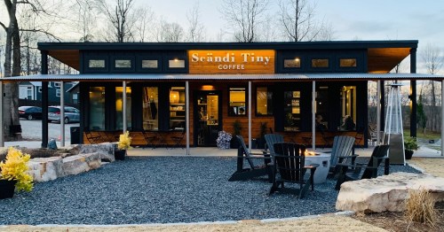 A modern coffee shop with a wooden exterior, outdoor seating, and a sign reading "Scändi Tiny Coffee" at dusk.