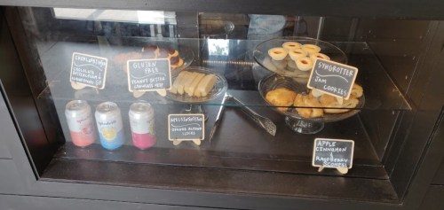 Display case with assorted baked goods, including gluten-free options, jam cookies, and flavored sodas.
