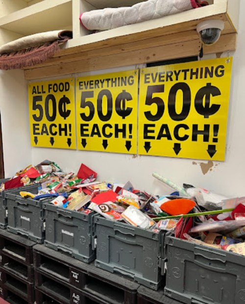 A cluttered display of items in bins with signs stating "All Food 50¢ Each!" and "Everything 50¢ Each!" on the wall.