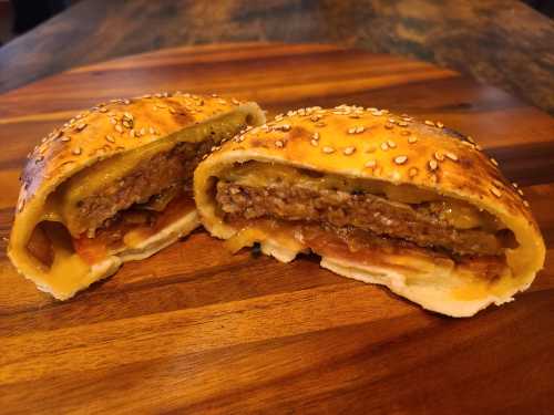 A sesame-seed topped pastry cut in half, revealing layers of meat, cheese, and vegetables inside.