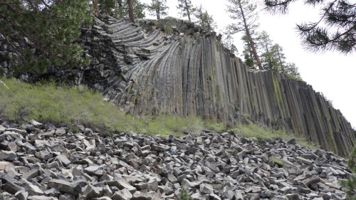 A rocky cliff with distinct vertical columns, surrounded by scattered boulders and sparse greenery.