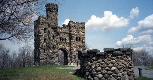 A stone castle with a tower and archway, surrounded by trees and a cloudy sky.