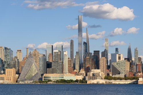 A skyline view of a modern city with diverse skyscrapers and a clear blue sky, reflecting on the water below.