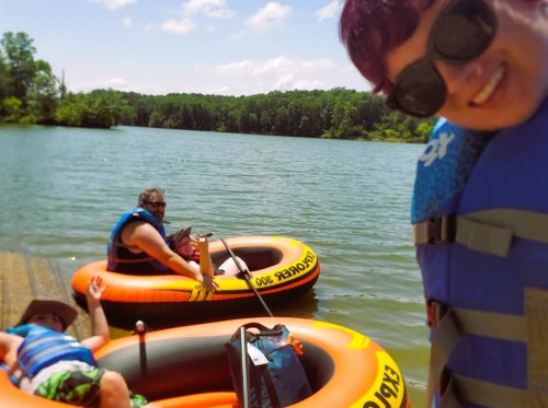 A group of friends relaxes on inflatable rafts by a lake, enjoying a sunny day outdoors.