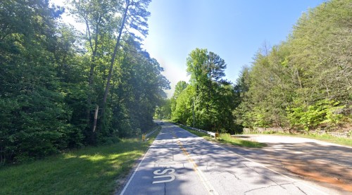 A winding road surrounded by lush green trees under a clear blue sky.