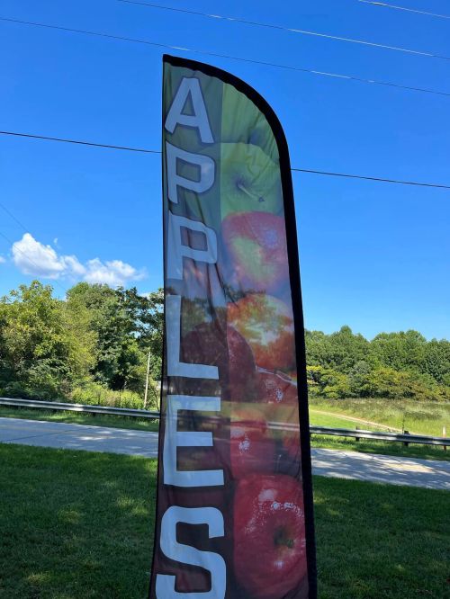 A tall banner displaying the word "APPLES" with images of apples against a blue sky and green trees in the background.