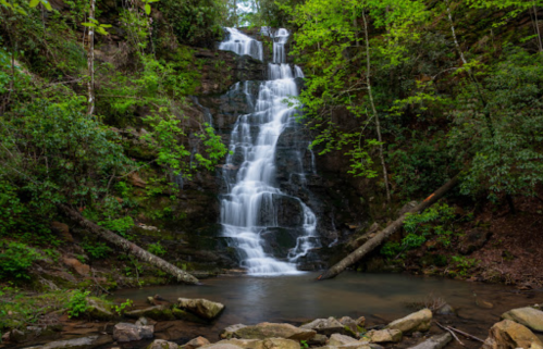 A serene waterfall cascading down rocky cliffs, surrounded by lush green trees and a calm pool at the base.