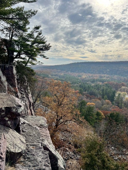 A scenic view from a rocky cliff overlooking a valley filled with autumn foliage and a cloudy sky.