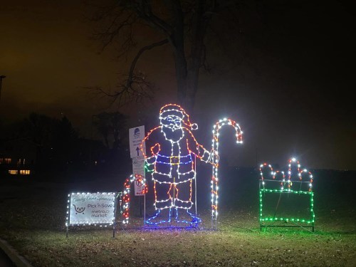 A festive display featuring a lit Santa Claus, a candy cane, and a gift box, set against a dark night sky.