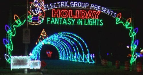 Colorful holiday lights form an archway reading "Holiday Fantasy in Lights" at night, with festive decorations visible.