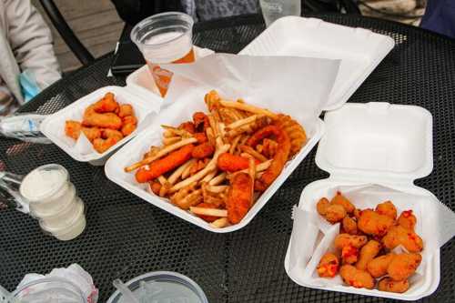 A table with three containers of fried food, including fries, chicken wings, and small corn dogs, alongside drinks.