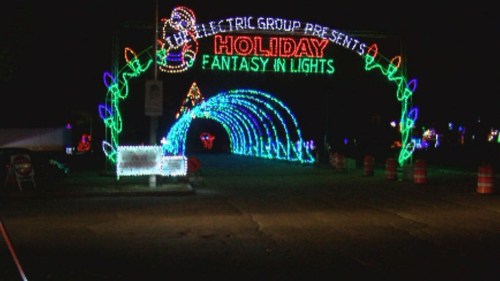 Colorful holiday lights form an archway reading "Holiday Fantasy in Lights" at night, with festive decorations.