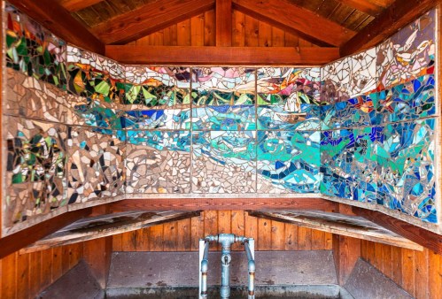 Mosaic artwork on a wooden wall, featuring colorful tiles depicting water and nature scenes.
