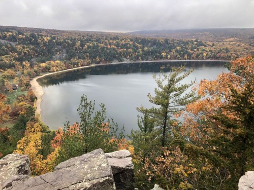 A serene lake surrounded by autumn foliage and rocky cliffs under a cloudy sky.
