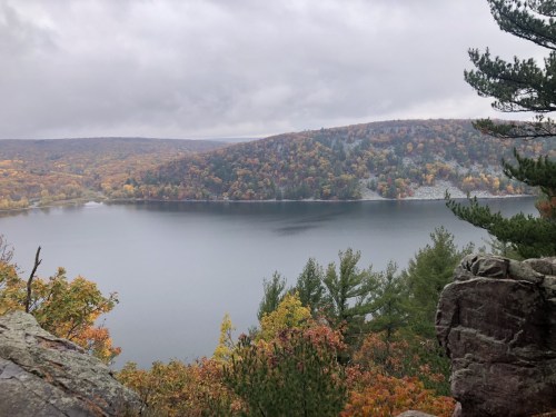 A serene lake surrounded by autumn foliage and rocky cliffs under a cloudy sky.