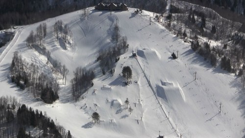 Aerial view of a snowy ski slope with trails, trees, and ski lifts on a mountain.