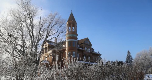 A large, ornate house with a tower, surrounded by frosty trees under a clear blue sky.