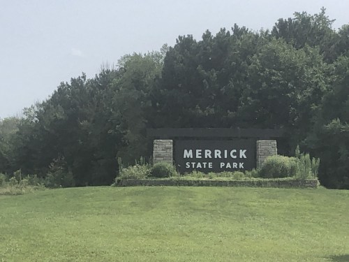 Sign for Merrick State Park surrounded by greenery and trees on a sunny day.