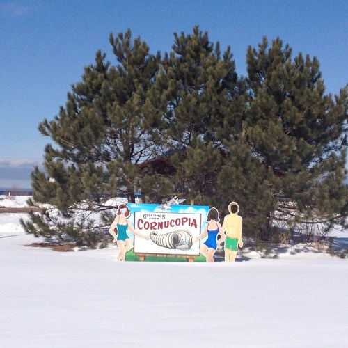 A colorful sign for "Gillingham's Cornucopia" with two cartoon figures in swimwear, set against a snowy landscape and trees.