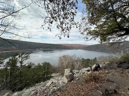 A serene lake surrounded by autumn foliage and rocky terrain, under a cloudy sky.