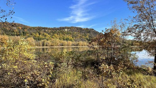 A serene lake surrounded by autumn foliage and a distant hill under a clear blue sky.
