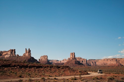 A scenic desert landscape with towering rock formations and a winding road, under a clear blue sky.