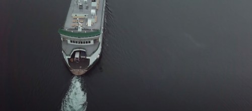 Aerial view of a ferry navigating through calm waters, leaving a wake behind it.
