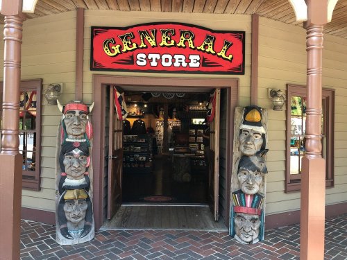 Entrance to a general store featuring colorful signage and carved wooden figures on either side of the doorway.