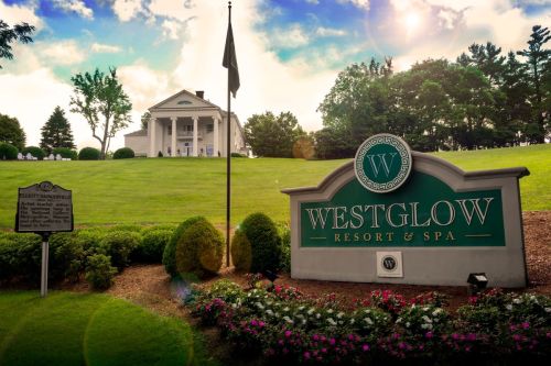 Sign for Westglow Resort & Spa in front of a lush green landscape and a historic building under a bright sky.