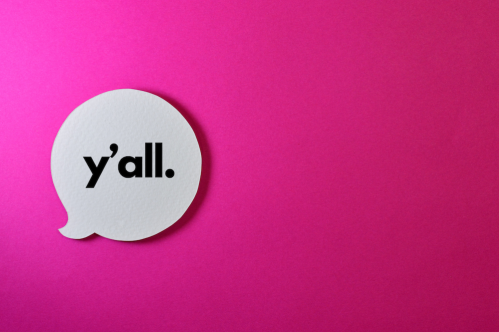 A white speech bubble on a pink background with the text "y'all." in bold black letters.