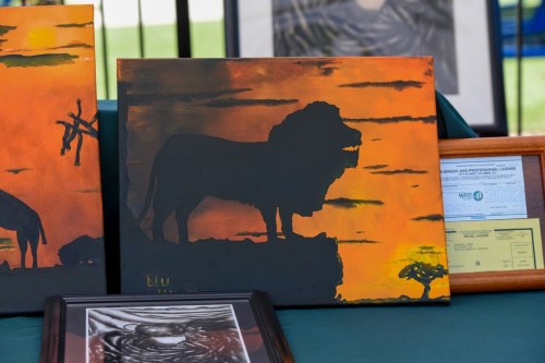 A silhouette of a lion against an orange sunset, displayed on an easel with other artwork in the background.