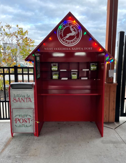 A festive red mailbox and kiosk for letters to Santa, decorated with lights, located in West Columbia.