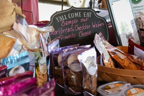 A display of various snacks, including shortbread, cheddar wafers, and pimento cheese, with a sign inviting samples.