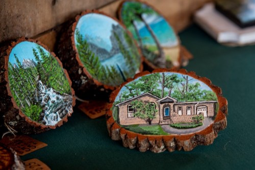 Hand-painted wooden coasters featuring scenic landscapes and a house, displayed on a green tablecloth.
