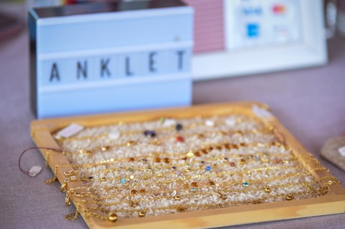 A display of colorful anklets on a textured surface, with a lightbox sign reading "ANKLET" in the background.