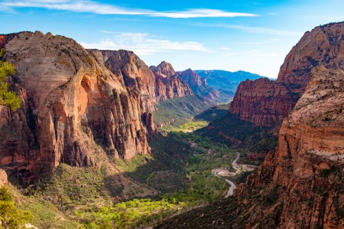 A panoramic view of Zion National Park, showcasing towering red rock cliffs and a lush green valley below.