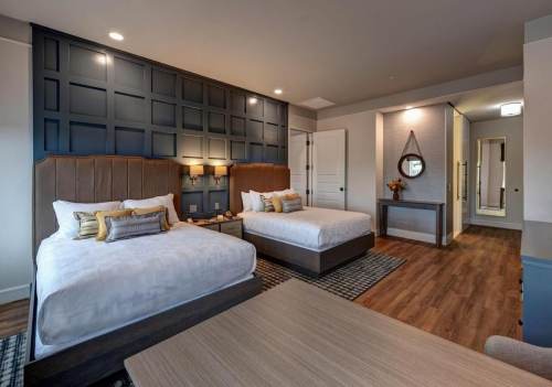 A modern hotel room featuring two beds, stylish decor, and a cozy seating area with wooden accents.