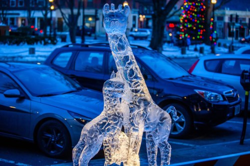 An ice sculpture of a raised hand, illuminated, with cars and festive lights in the background.