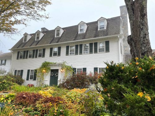 A charming white house with green shutters, surrounded by colorful autumn foliage and a misty atmosphere.