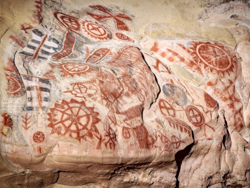Ancient rock art featuring various red and black geometric patterns and symbols on a stone surface.