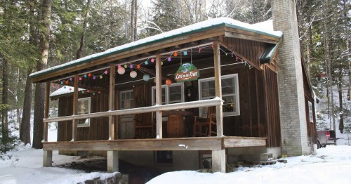 A cozy wooden cabin in a snowy forest, decorated with colorful lights and a welcoming porch.