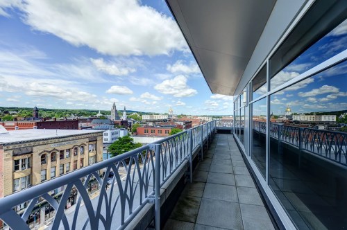 A balcony view overlooking a cityscape with buildings and a blue sky dotted with clouds.
