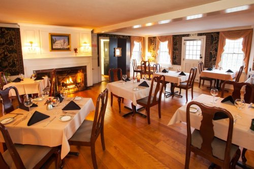 Cozy restaurant interior with wooden tables, chairs, and a fireplace, featuring elegant decor and a warm atmosphere.