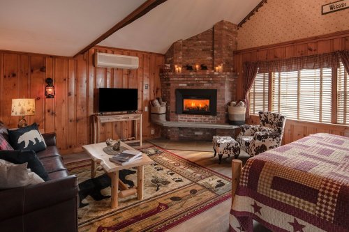 Cozy cabin interior with wooden walls, a fireplace, a TV, and rustic furniture, featuring a warm and inviting atmosphere.