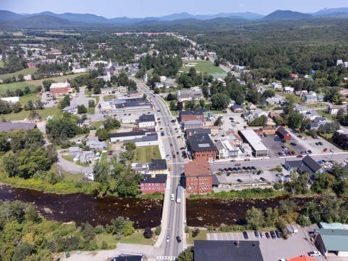 Aerial view of a small town with a river, green hills, and a mix of residential and commercial buildings.