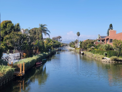 A serene canal lined with lush greenery and colorful homes under a clear blue sky.