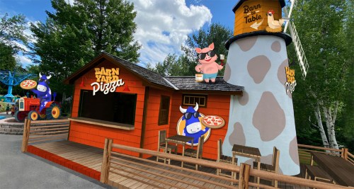 A colorful pizza stand with a barn theme, featuring cartoon animals and a tower, set in a park-like environment.