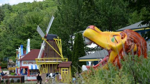 Colorful amusement park scene featuring a lion statue, a windmill, and whimsical buildings surrounded by greenery.