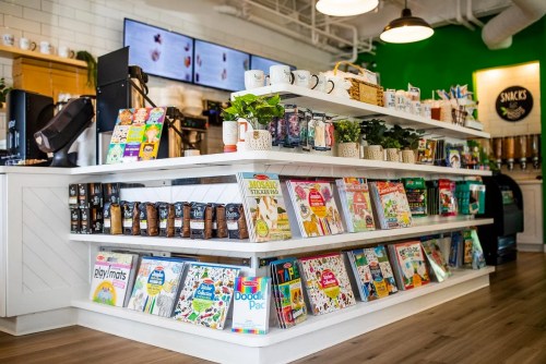 A bright café display featuring shelves of colorful books, snacks, and coffee equipment in a modern setting.